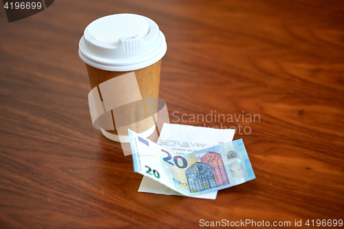 Image of coffee in paper cup, bill and money on table