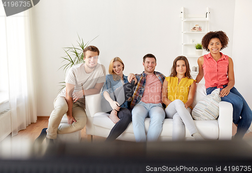 Image of happy friends with remote watching tv at home
