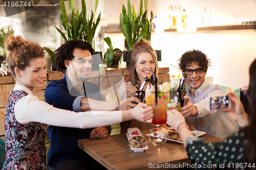 Image of happy friends clinking drinks at bar or cafe