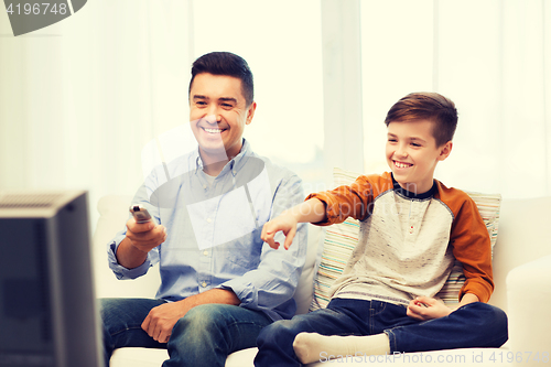 Image of smiling father and son watching tv at home