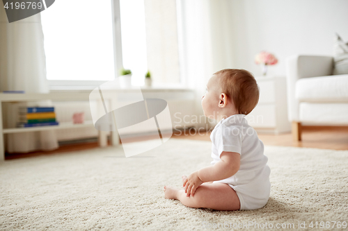 Image of happy baby boy or girl sitting on floor at home