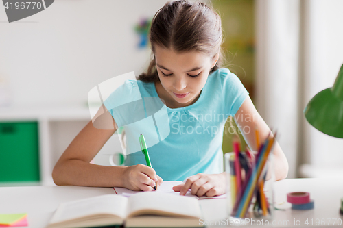 Image of happy girl with book writing to notebook at home