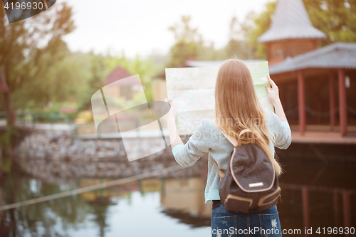 Image of Back side of traveler girl searching right direction on map, orange sunset light, traveling along Europe