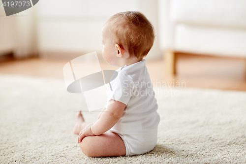 Image of happy baby boy or girl sitting on floor at home