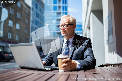 Image of senior businessman with laptop drinking coffee