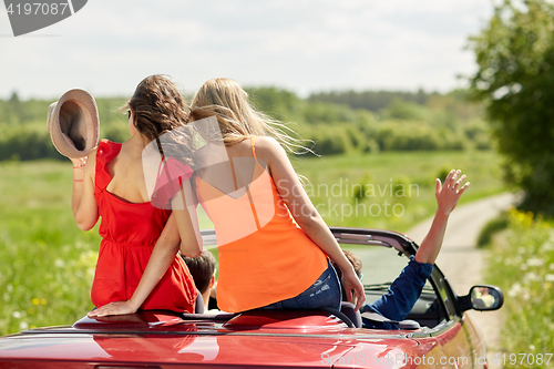 Image of happy friends driving in cabriolet car at country