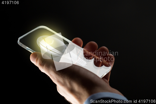 Image of close up of hand with lightbulb on smartphone