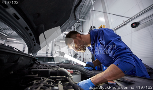 Image of mechanic man with lamp repairing car at workshop
