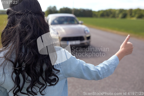 Image of woman hitchhiking and stopping car with thumbs up