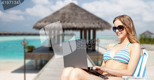 Image of happy young woman in shades with laptop on beach