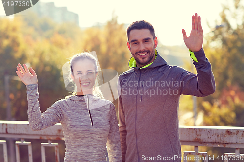 Image of smiling couple waving hand outdoors