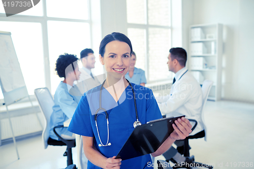 Image of happy doctor with clipboard over group of medics