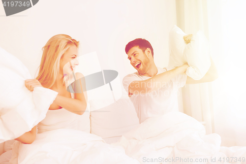 Image of happy couple having pillow fight in bed at home