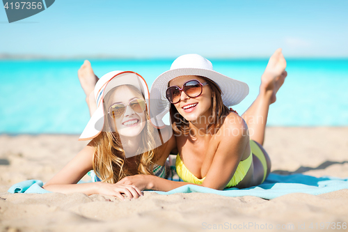 Image of happy women in hats sunbathing on beach
