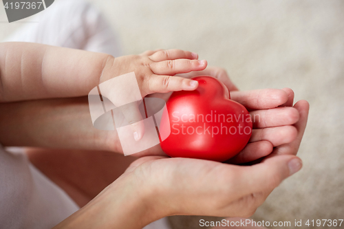 Image of close up of baby and mother hands with red heart