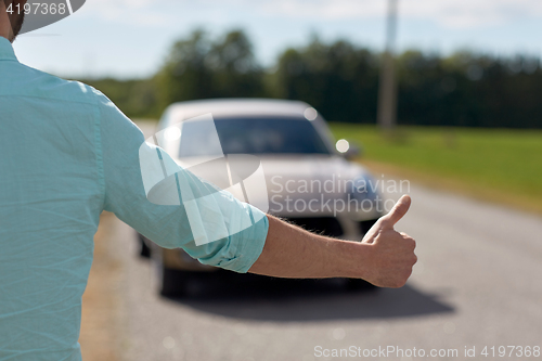 Image of man hitchhiking and stopping car with thumbs up