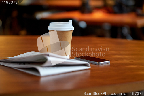 Image of coffee cup, smartphone and newspaper on cafe table