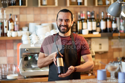 Image of happy man or waiter with bottle of red wine at bar