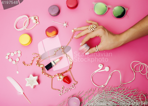 Image of woman hands holding macaroons with lot of girl stuff on pink background, girls accessories concept 