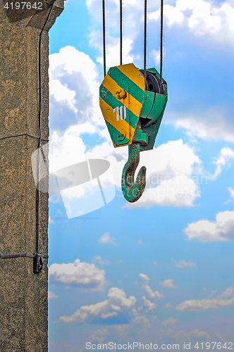Image of Yellow-green hook of a construction crane on a rope on a background of clouds