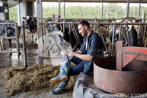 Image of young man with tablet pc and cows on dairy farm