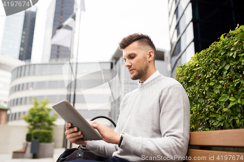 Image of man with tablet pc sitting on city street bench