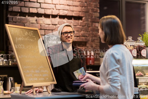 Image of happy barman and woman paying money at cafe