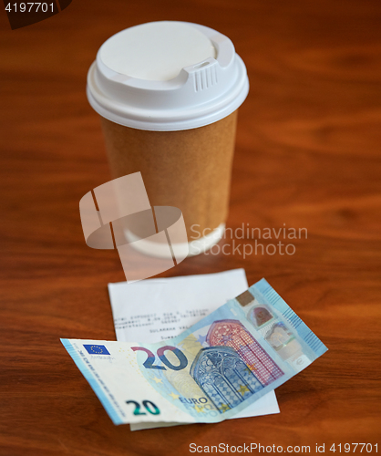 Image of coffee in paper cup, bill and money on table