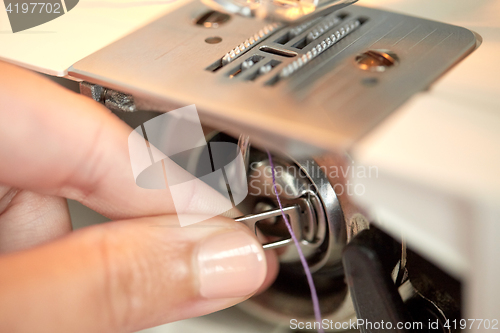 Image of tailor hand setting spool to sewing machine