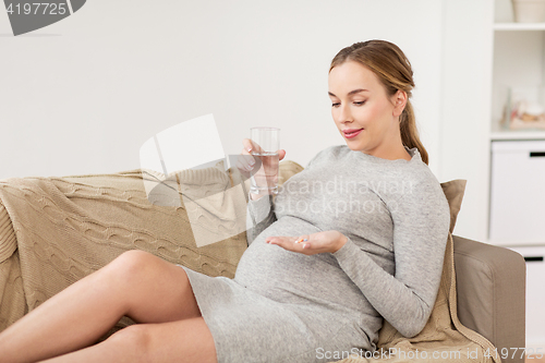 Image of happy pregnant woman with water and pills at home