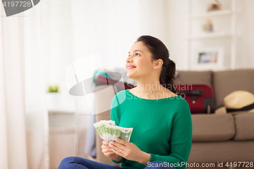 Image of happy woman with money and travel bag at home