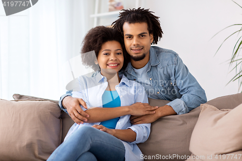 Image of happy couple sitting on sofa and hugging at home