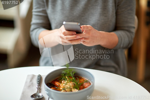 Image of woman with smartphone and bowl of soup at cafe