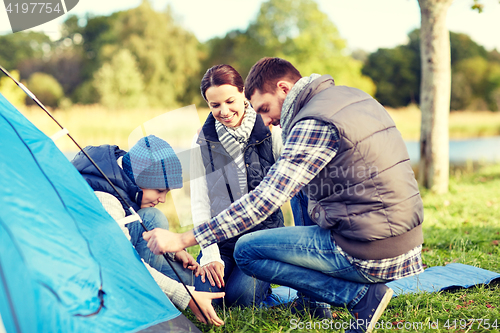 Image of happy parents and son setting up tent outdoors