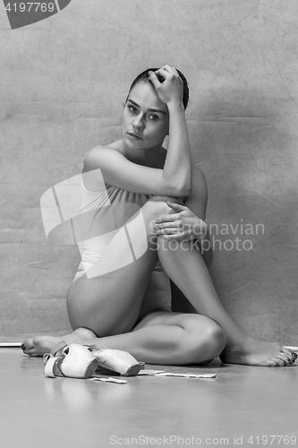 Image of Tired ballet dancer sitting on the wooden floor on a pink background