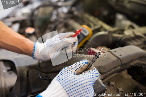 Image of auto mechanic man with multimeter testing battery