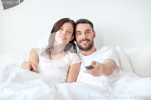 Image of happy couple lying in bed at home and watching tv