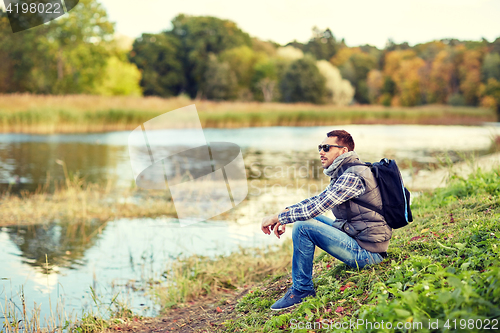 Image of man with backpack resting on river bank
