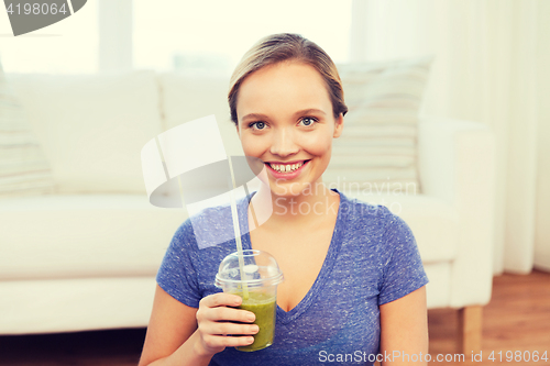 Image of happy woman with smoothie sitting on mat at home