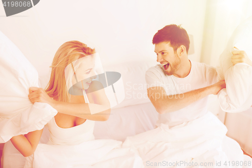 Image of happy couple having pillow fight in bed at home