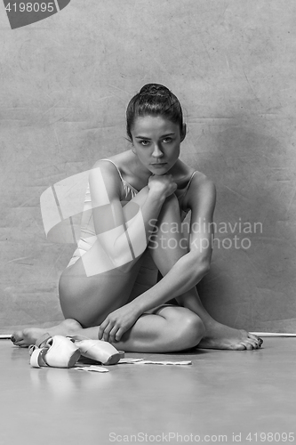 Image of Tired ballet dancer sitting on the wooden floor on a pink background