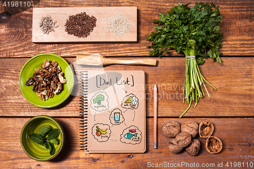 Image of Notebook for recipes, walnuts, parsley and seeds on wooden table.