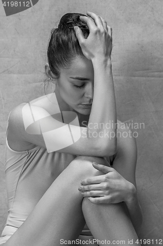 Image of Tired ballet dancer sitting on the wooden floor on a pink background