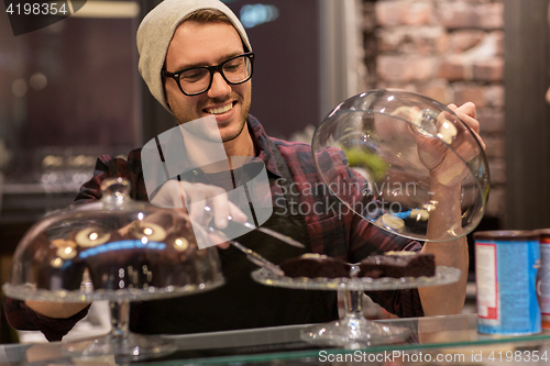 Image of man or barman with cakes and tongs at cafe counter