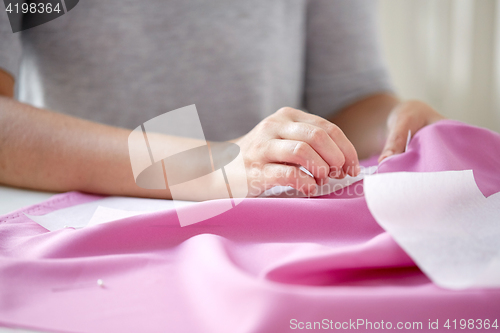 Image of woman with pins stitching paper pattern to fabric