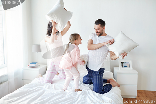 Image of happy family having pillow fight in bed at home