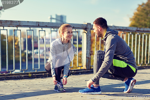 Image of smiling couple tying shoelaces outdoors