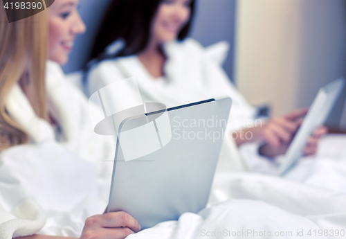 Image of happy women in bathrobes with tablet pc at hotel