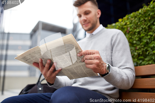 Image of man reading newspaper on city street bench