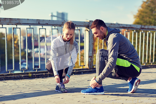 Image of smiling couple tying shoelaces outdoors